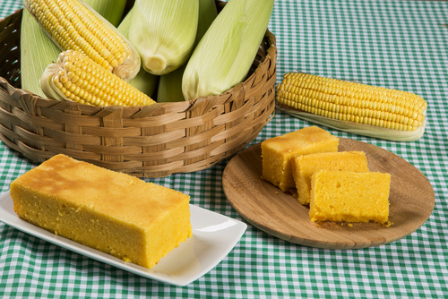 bolo de milho em pratos com uma cesta com espigas de milhos atrás - comidas típicas de São João - Assaí Atacadista