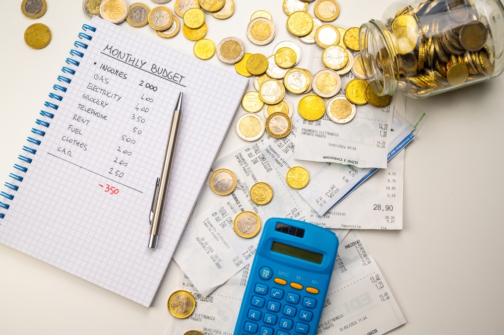 caderno com orçamento familiar, moedas espalhadas e uma calculadora - economia doméstica - Assaí Atacadista