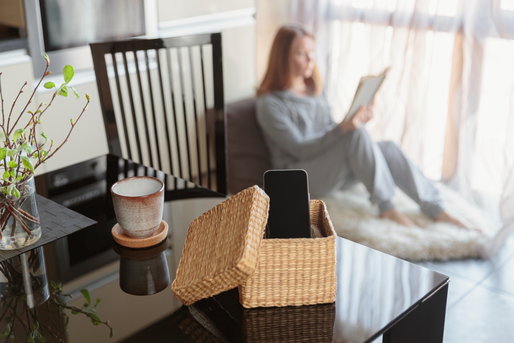 celular em um organizador em uma mesa com uma mulher branca no fundo lendo um livro - descansar nas férias - Assaí Atacadista