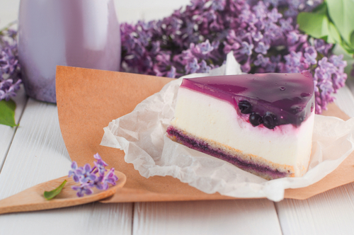 cheesecake com uma geleia roxa em um prato em uma mesa branca com flores no fundo - Assaí Atacadista - receitas com açaí