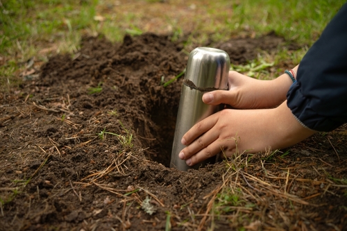 criança branca enterrando uma cápsula do tempo na terra - férias escolares - Assaí Atacadista