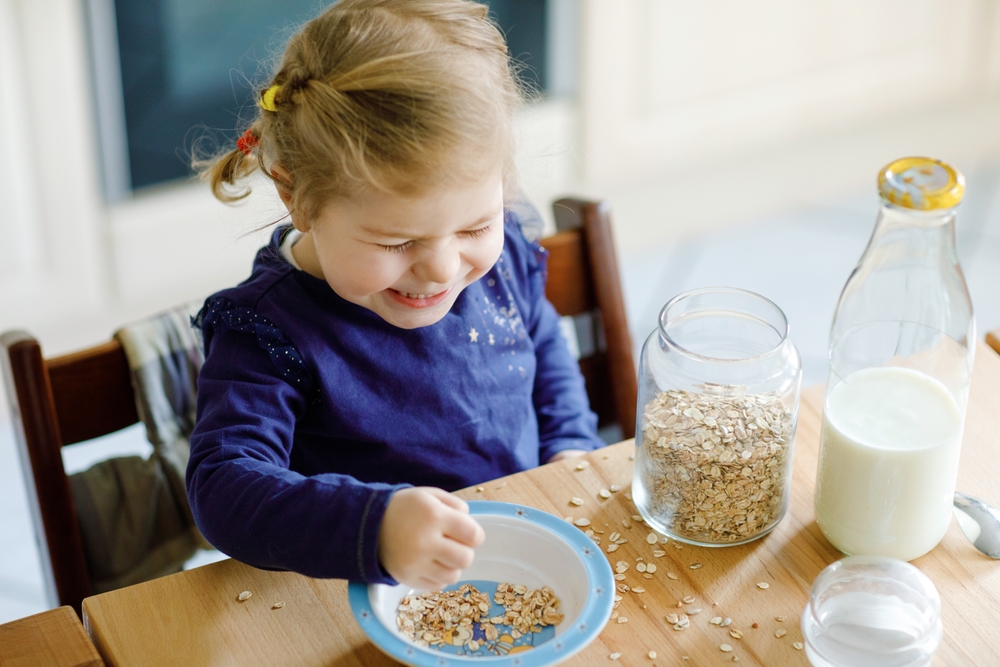 criança branca feliz comendo aveia na mesa - Assaí Atacadista - Mucilon