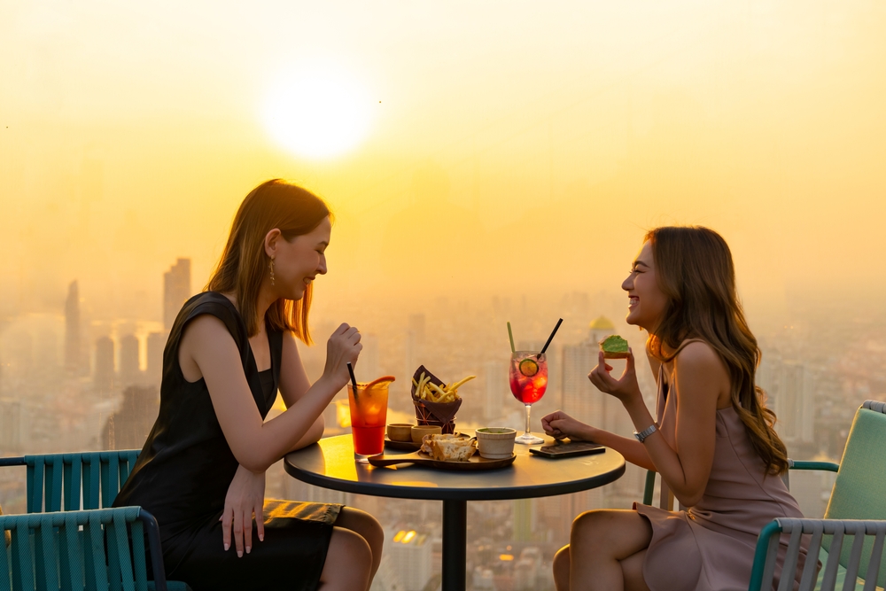 duas mulheres asiáticas felizes jantando ao pôr do sol - experiências gastronômicas - Assaí Atacadista