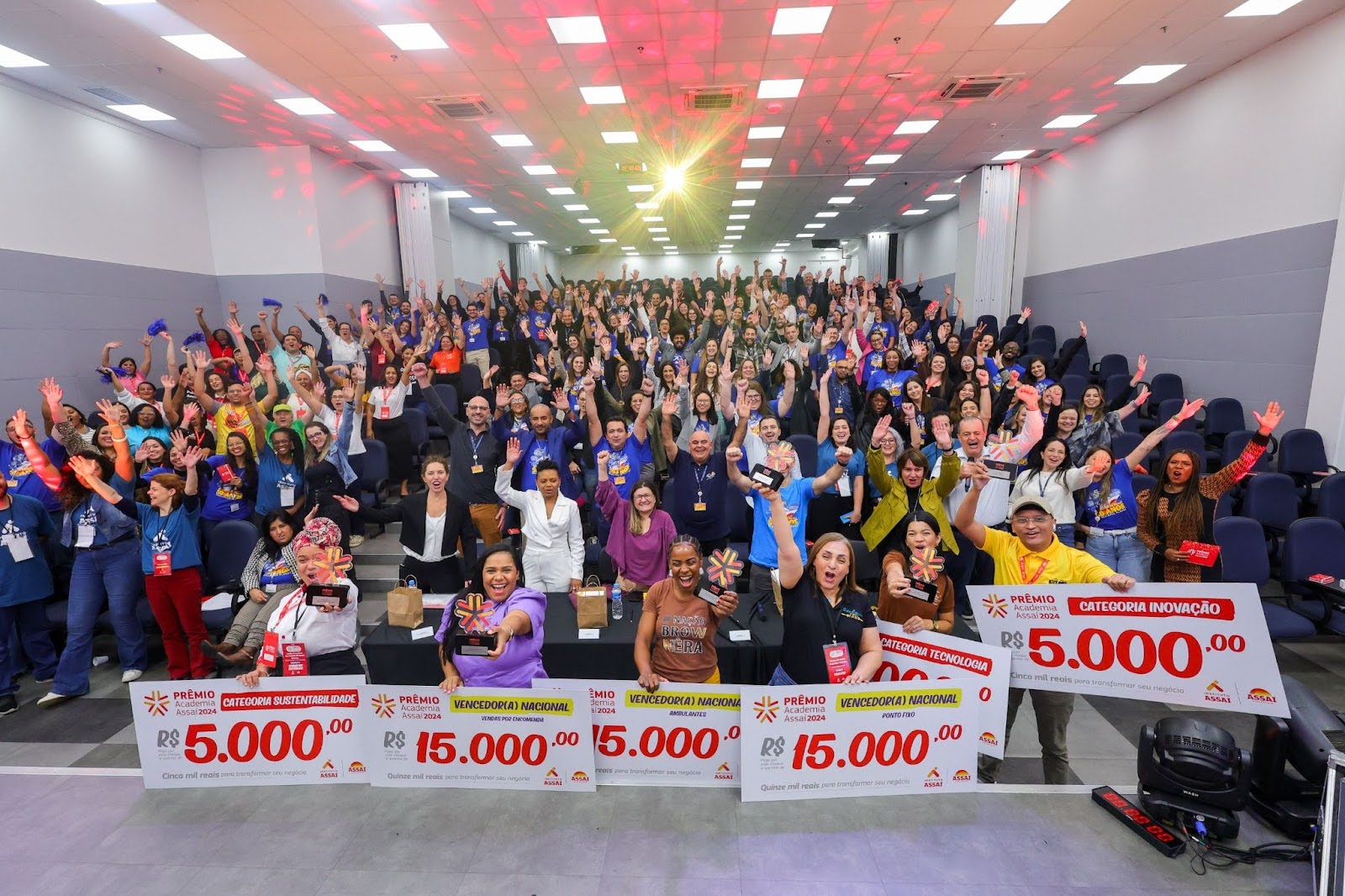 foto de um auditótio cheio de pessoas com os braços pra cima, com os ganhadores do Prêmio Academia Assaí 2024 na frente - Instituto Assaí Atacadista