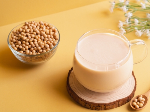 fundo amarelo com uma xícara com leite de soja e uma tigela com grãos de soja - bebidas vegetais - Assaí Atacadista