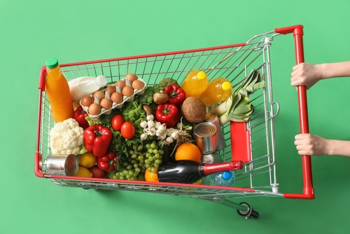 fundo verde com um carrinho de supermercado cheio de alimentos - Assaí Atacadista - cesta básica