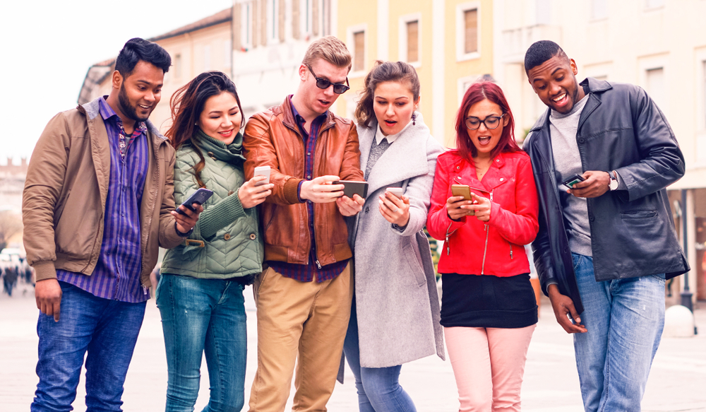 grupo de homens e mulheres diversos olhando para os celulares em suas mãos - Assaí Atacadista - recesso de Ano-Novo