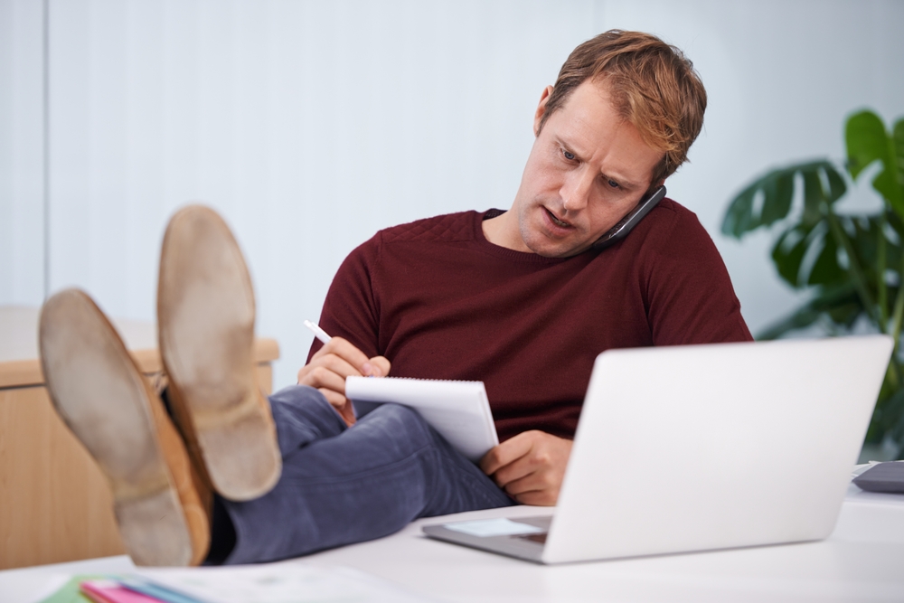 homem branco falando no celular enquanto anota em um bloco de notas - economia doméstica - Assaí Atacadista