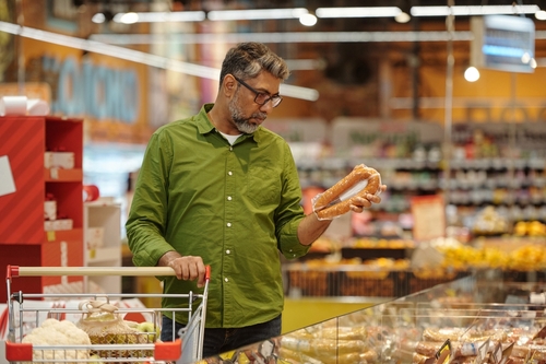 homem de meia-idade em um mercado segurando um produto com uma mão e o carrinho de compras com outra - redução de custos - Assaí Atacadista