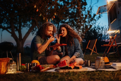 homem e mulher sentados no chão lanchando com itens de piquenique - atividades noturnas - Assaí Atacadista - Imagem: Shutterstock