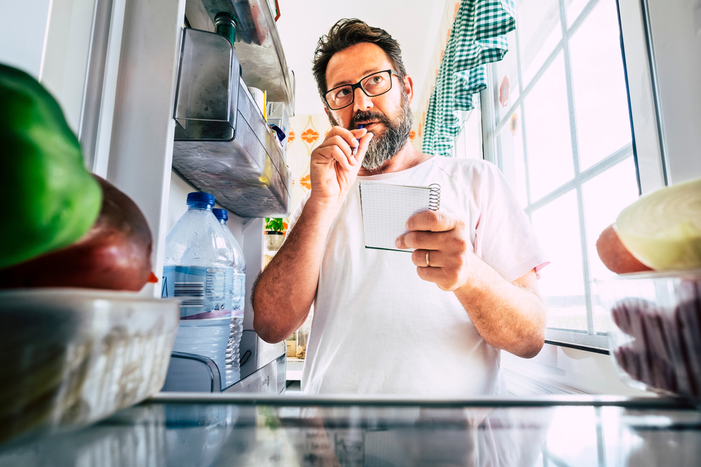 homem fazendo lista de compras com a geladeira aberta - economizar nas compras - Assaí Atacadista