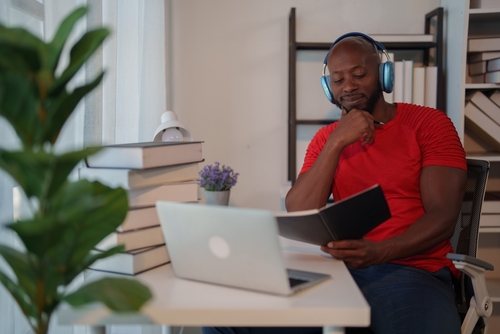 homem negro contente em um escritório estudando com um livro e um notebook - snacks para crianças - Assaí Atacadista