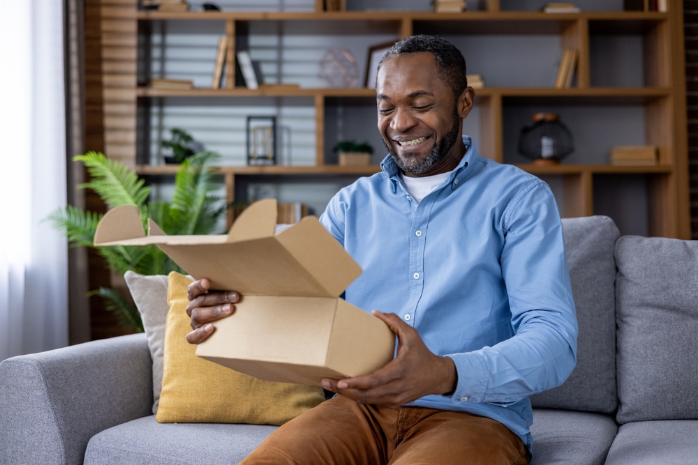 homem negro da terceira idade segurando uma caixa aberta enquanto sorri olhando pra ela - Assaí Atacadista - delivery natalino