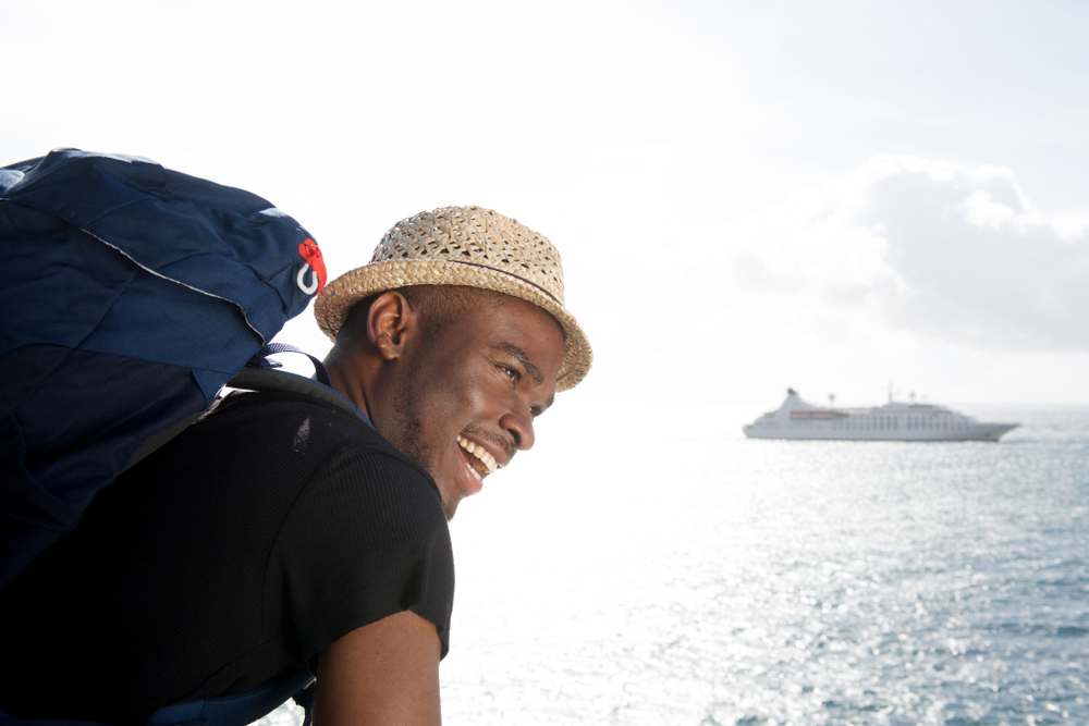 homem negro feliz com mala nas costas olhando para um navio - viagem de navio - Assaí Atacadista