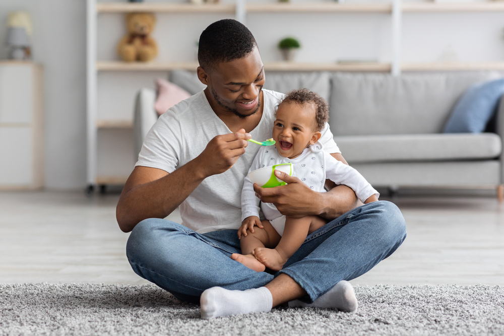homem negro feliz dando papinha para um bebê - Assaí Atacadista - Mucilon