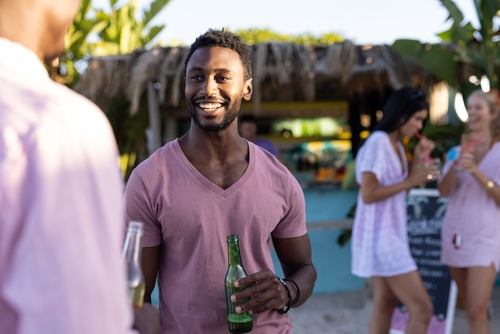 homem negro feliz tomando uma bebida na praia com amigos - vendas de verão - Assaí Atacadista