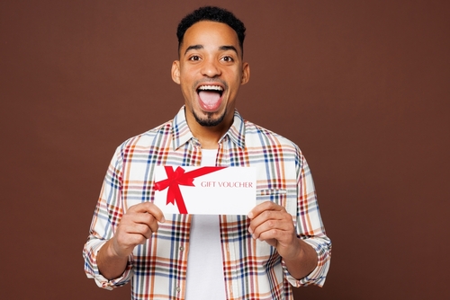 homem negro jovem feliz segurando um voucher de presente nas mãos - Assaí Atacadista - cortesia de aniversário