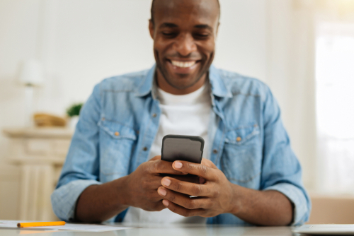 homem negro sorrindo usando o celular-assai no ifood-Assaí Atacadista