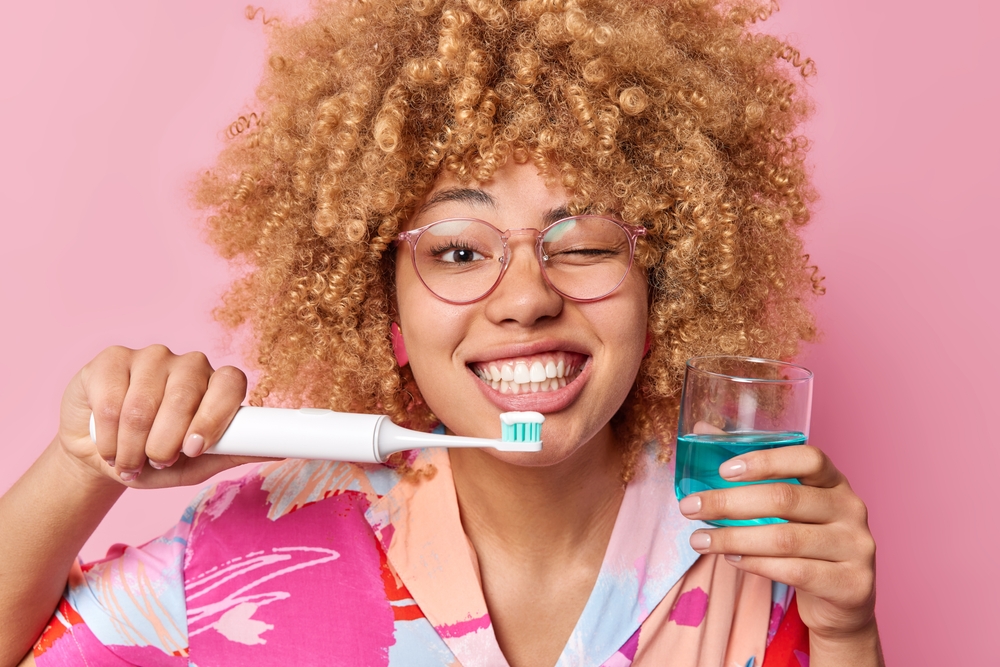 jovem negra sorrindo com escova de dente e um enxaguantem ultra action nas mãos - Assaí Atacadista
