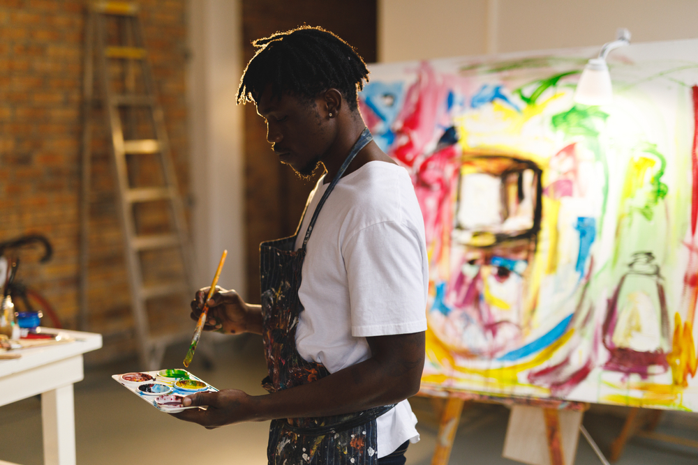 jovem negro concentrado misturando tintas em uma paleta para pintar um quadro - o que fazer no verão - Assaí Atacadista