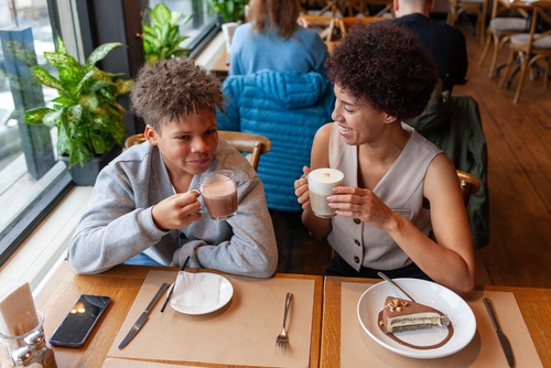 mãe e filho negros tomando café felizes em um estabelecimento - evento de Dia das Mães - Assaí Atacadista