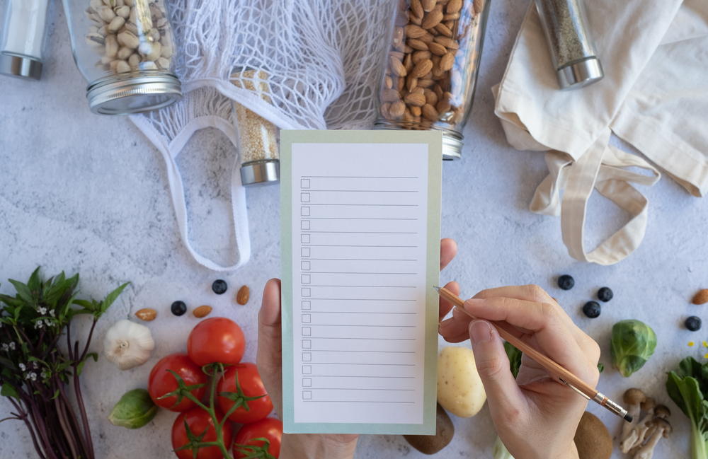 mão segurando bloco de notas com alimentos em volta - estoque de alimentos - Assaí Atacadista