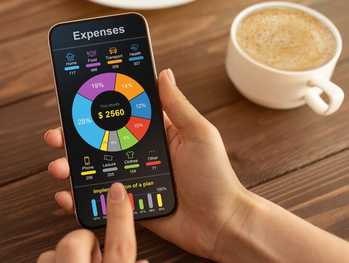 mãos brancas segurando um celular com um gráfico de pizza e informações financeiras em uma mesa com uma xícara de café ao lado - redução de custos - Assaí Atacadista