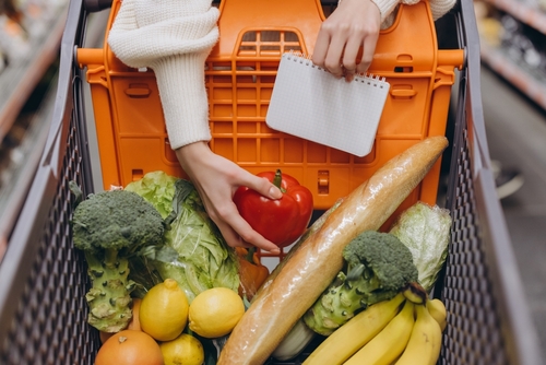 mãos de uma pessoa branca apoiada em um carrinho de supermercado com alimentos dentro - marmitas semanais - Assaí Atacadista