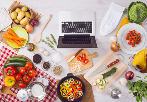 mesa branca com vários legumes e verduras espalhados em pratos, tigelas e tábuas com um notebook no meio - marmitas semanais - Assaí Atacadista