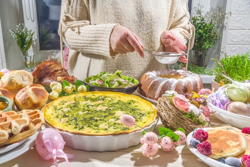 mesa cheia de pratos de Páscoa com uma pessoa branca enfeitando um bolo - cardápio de Páscoa - Assaí Atacadista