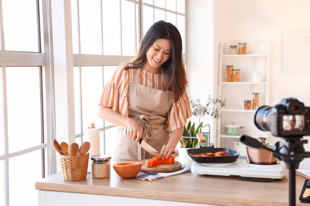 mulher asiática sorrindo enquanto cozinha e grava - comida afetiva - Assaí Atacadista