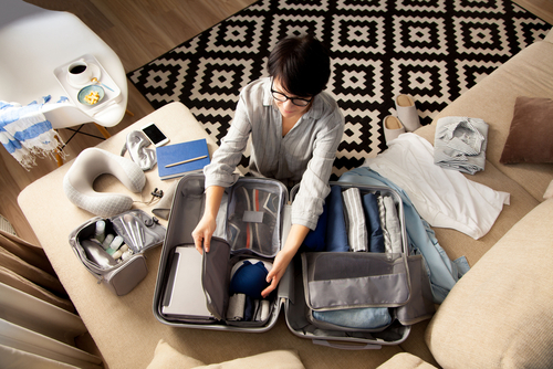 mulher branca organizando uma mala de viagem no sofá - bate-volta - Assaí Atacadista