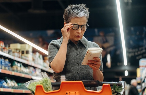 mulher branca sênior segurando o óculos e olhando para uma caderneta em um mercado - voltar a economizar - Assaí Atacadista