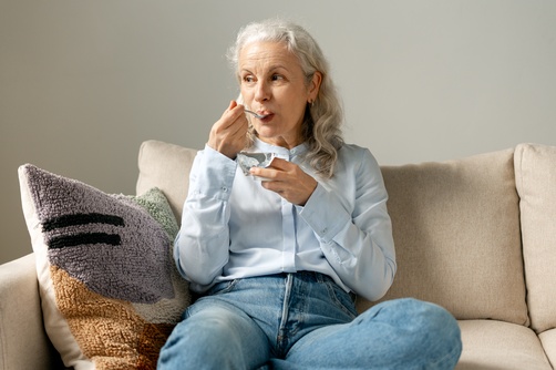 mulher branca sênior sentada em um sofá comendo - lista de compras - Assaí Atacadista