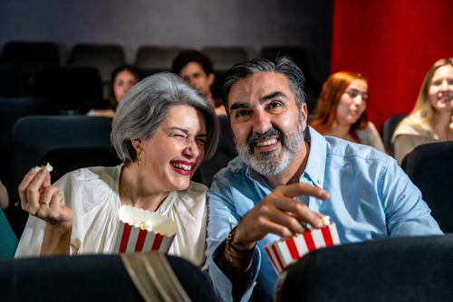 mulher e homem brancos idosos sorrindo em uma sala de cinema comendo pipoca - Assaí Atacadista - aniversário sem festa