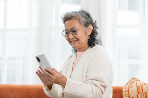 mulher idosa sorrindo usando um celular nas mãos - Assaí Atacadista - cortesia de aniversário