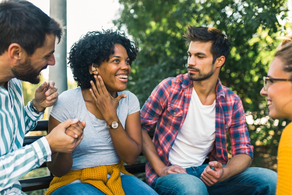 mulher jovem negra com aparelho auditivo com amigos - Assaí Atacadista - pessoas com deficiência