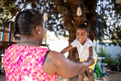 mulher negra brincando com uma criança em um parquinho dando as mãos - acomodações de Carnaval - Assaí Atacadista - Imagem: Shutterstock