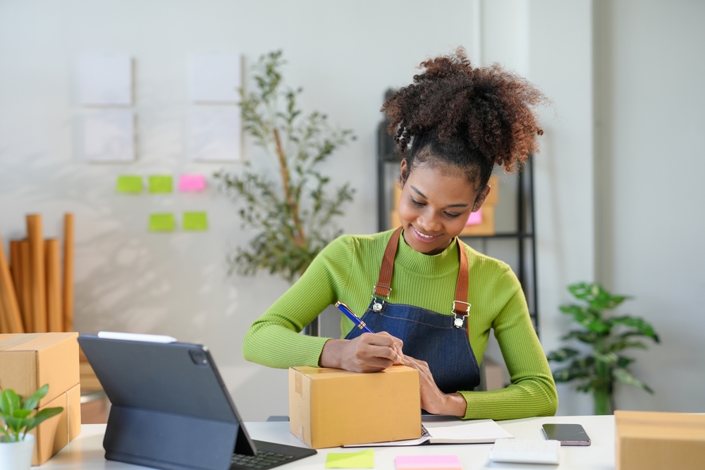 mulher negra empreendedora alegre escrevendo em uma caixa em um escritório - Assaí Atacadista - experiência do cliente 