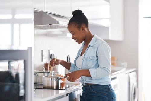 mulher negra feliz cozinhando - dicas de cozinha para quem mora sozinho - Assaí Atacadista