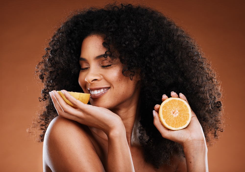 mulher negra sorrindo segurando laranjas nas mãos - beleza e alimentação - Assaí Atacadista
