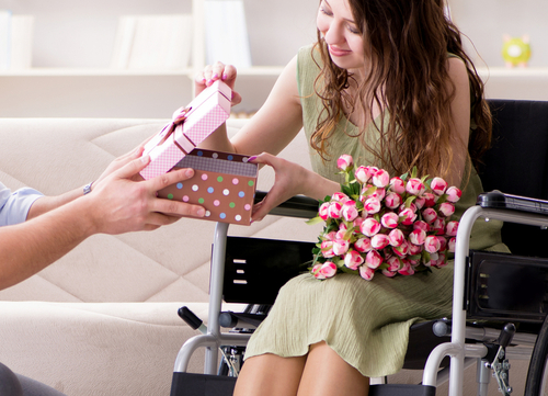 mulher PCD cadeirante recebendo flores e uma caixa de presente no Dia da Mulher - Assaí Atacadista