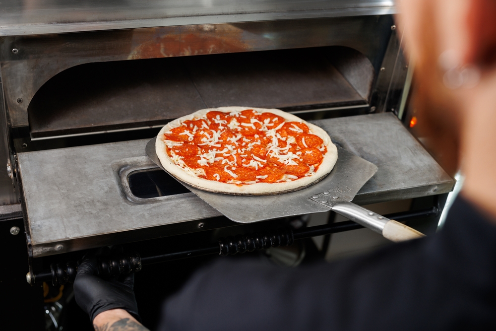 pessoa colocando a pizza no forno - abrir uma pizzaria - Assaí Atacadista