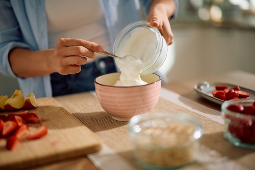 pessoa colocando iogurte em uma tigela com frutas na mesa-Assaí Atacadista-Danone