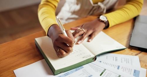 pessoa negra escrevendo em um caderno com papéis na mesa - voltar a economizar - Assaí Atacadista
