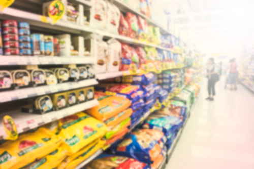 prateleiras de mercado com produtos para pet, como grandes pacotes de ração, latas e outros em uma imagem desfocada - economizar com pets - Assaí Atacadista