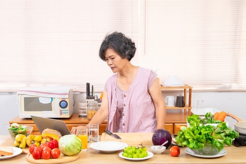senhora asiática séria olhando para um notebook na bancada de uma mesa com alimentos diversos - snacks para crianças - Assaí Atacadista