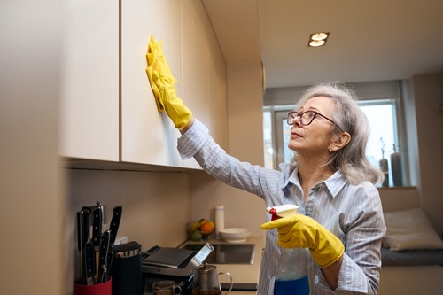 senhora branca da terceira idade limpando o gabinete da cozinha com uma flanela e um borrifador - limpeza da cozinha - Assaí Atacadista