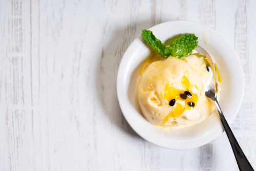 sorvete de maracujá em um pote branco em um fundo branco com uma colher - receitas de doces - Assaí Atacadista