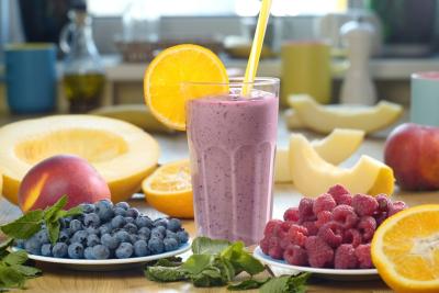 copo com bebida roxa e fatia de laranja na borda em uma mesa com frutas diversas - smoothies energéticos - Assaí Atacadista